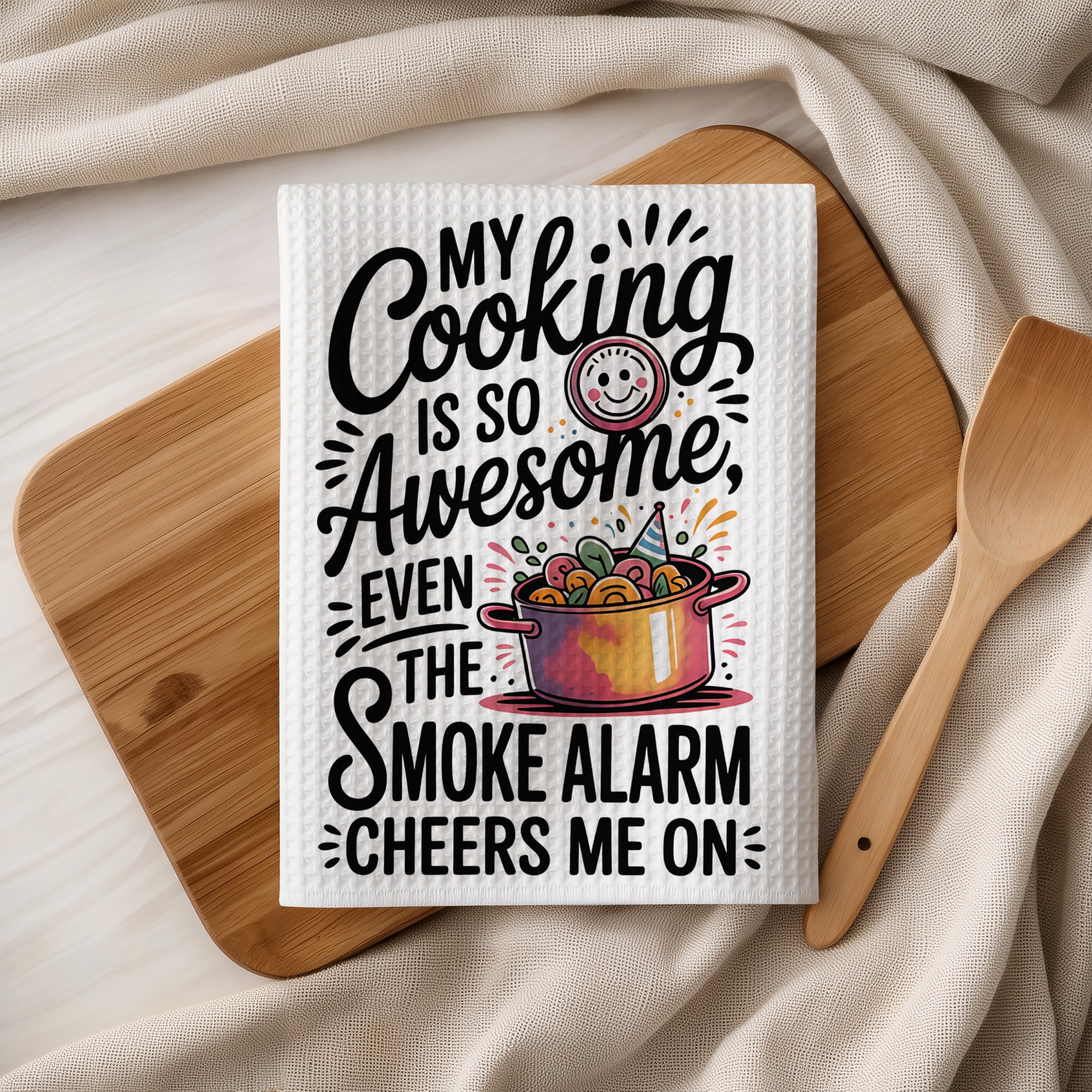 White kitchen towel with "My Cooking is So Awesome Even the Smoke Alarm Cheers Me On" text.