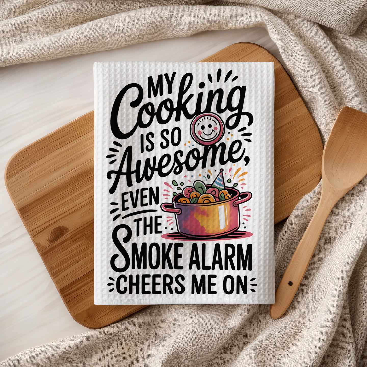 White kitchen towel with "My Cooking is So Awesome Even the Smoke Alarm Cheers Me On" text.