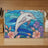 Stained glass art of a dolphin leaping through water, surrounded by flowers.