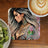 Coaster with tattooed woman and "Be The Light" text, beside coffee and kiwi.