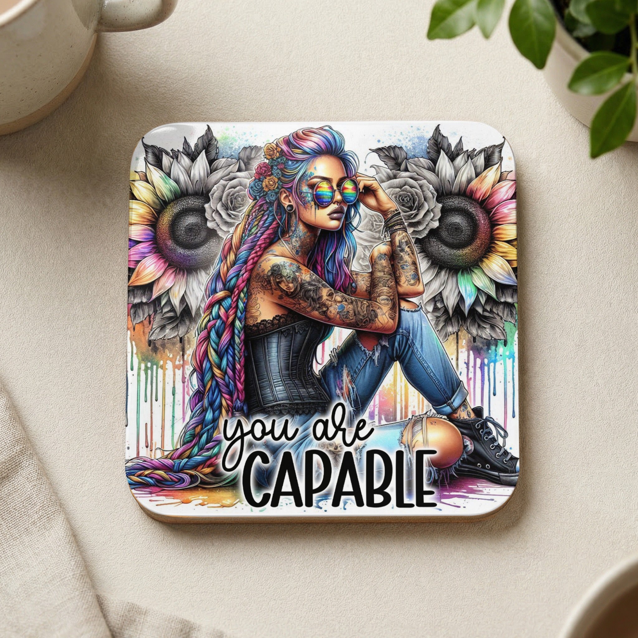 Woman with colorful braided hair, tattoos, and sunglasses sits with "you are capable" text.