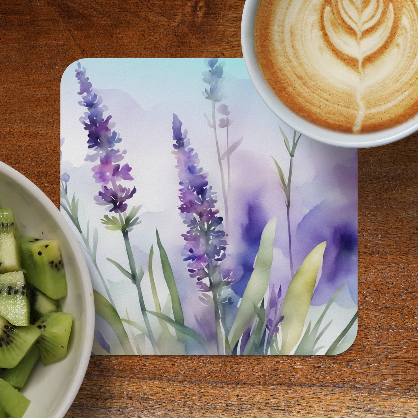 Watercolor lavender painting on a coaster next to kiwi and coffee.