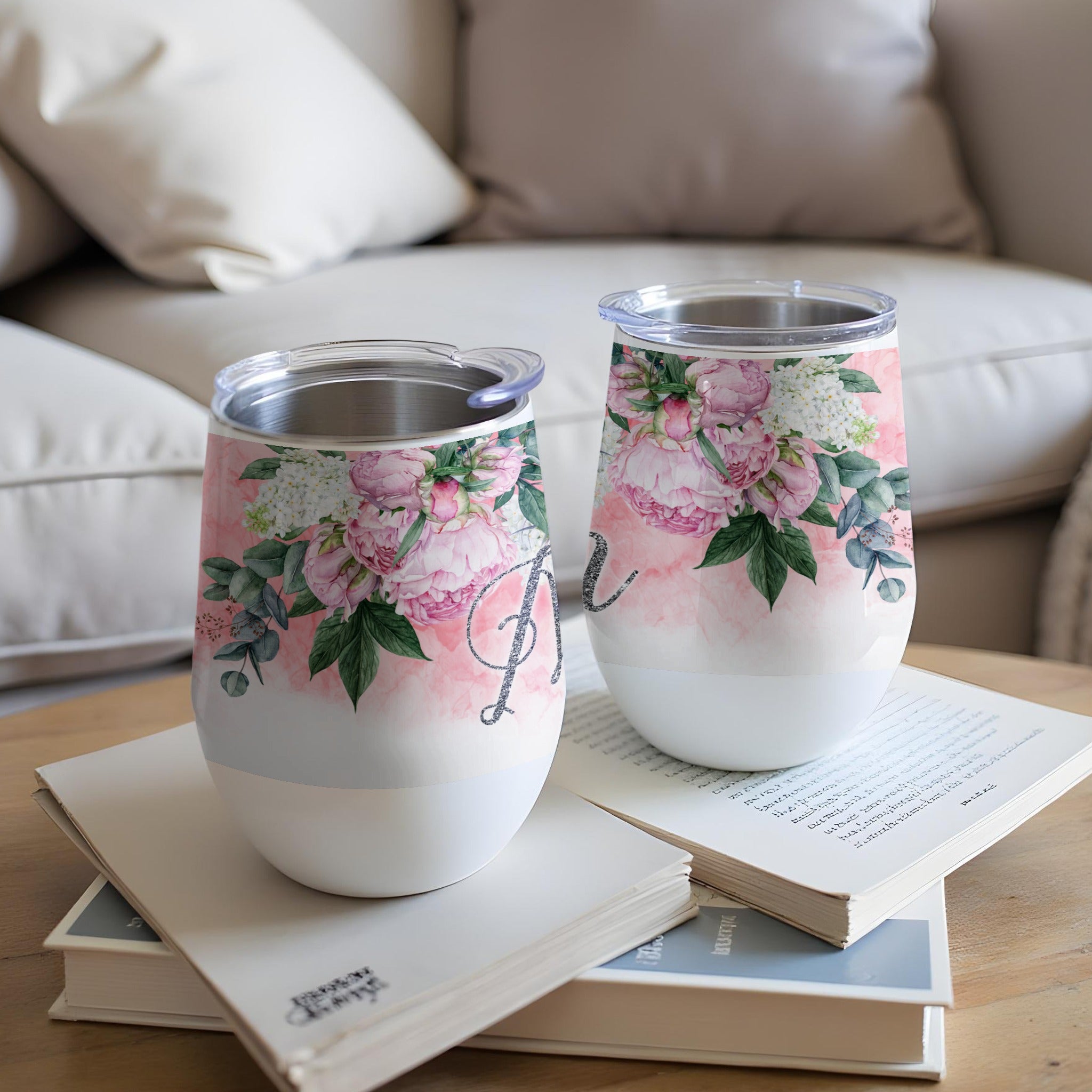 Two floral patterned wine tumblers with silver lids sit on books.