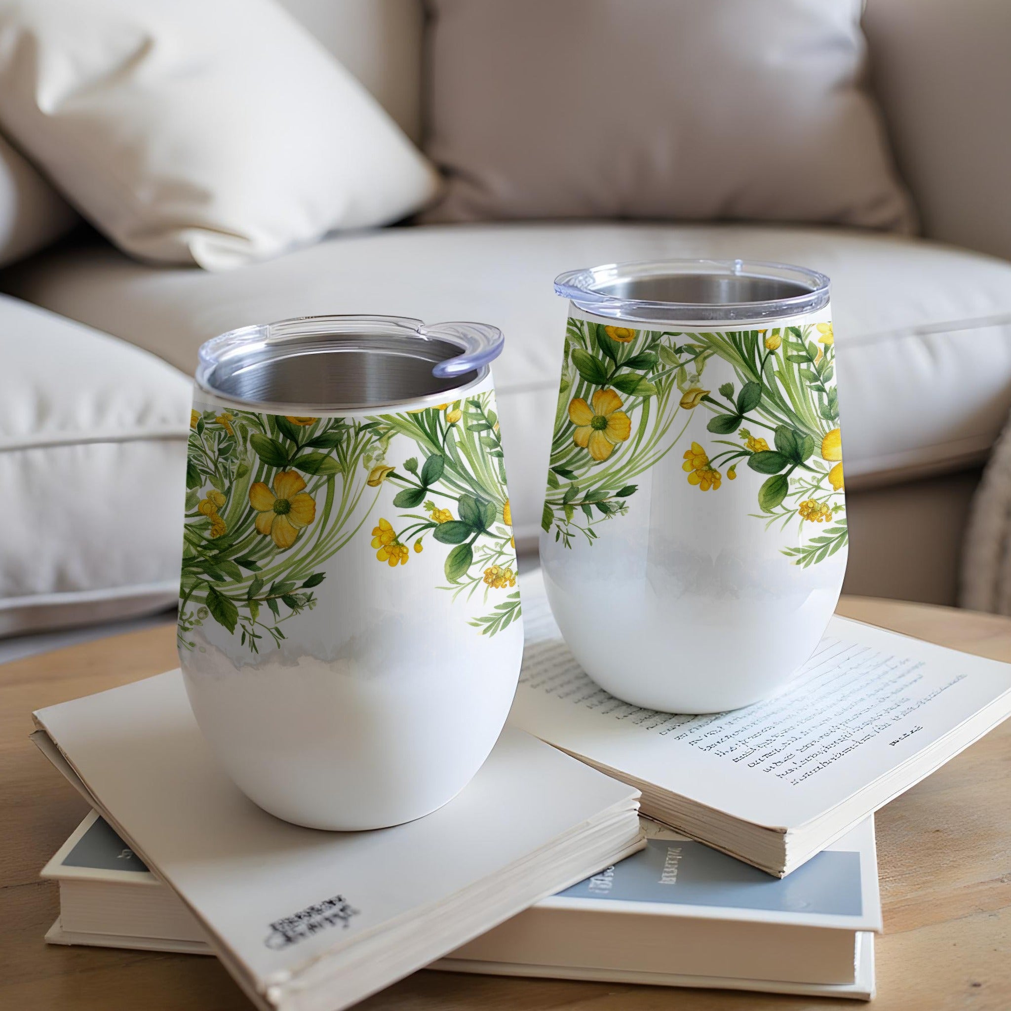 Two white tumblers with green foliage and yellow flowers on books.