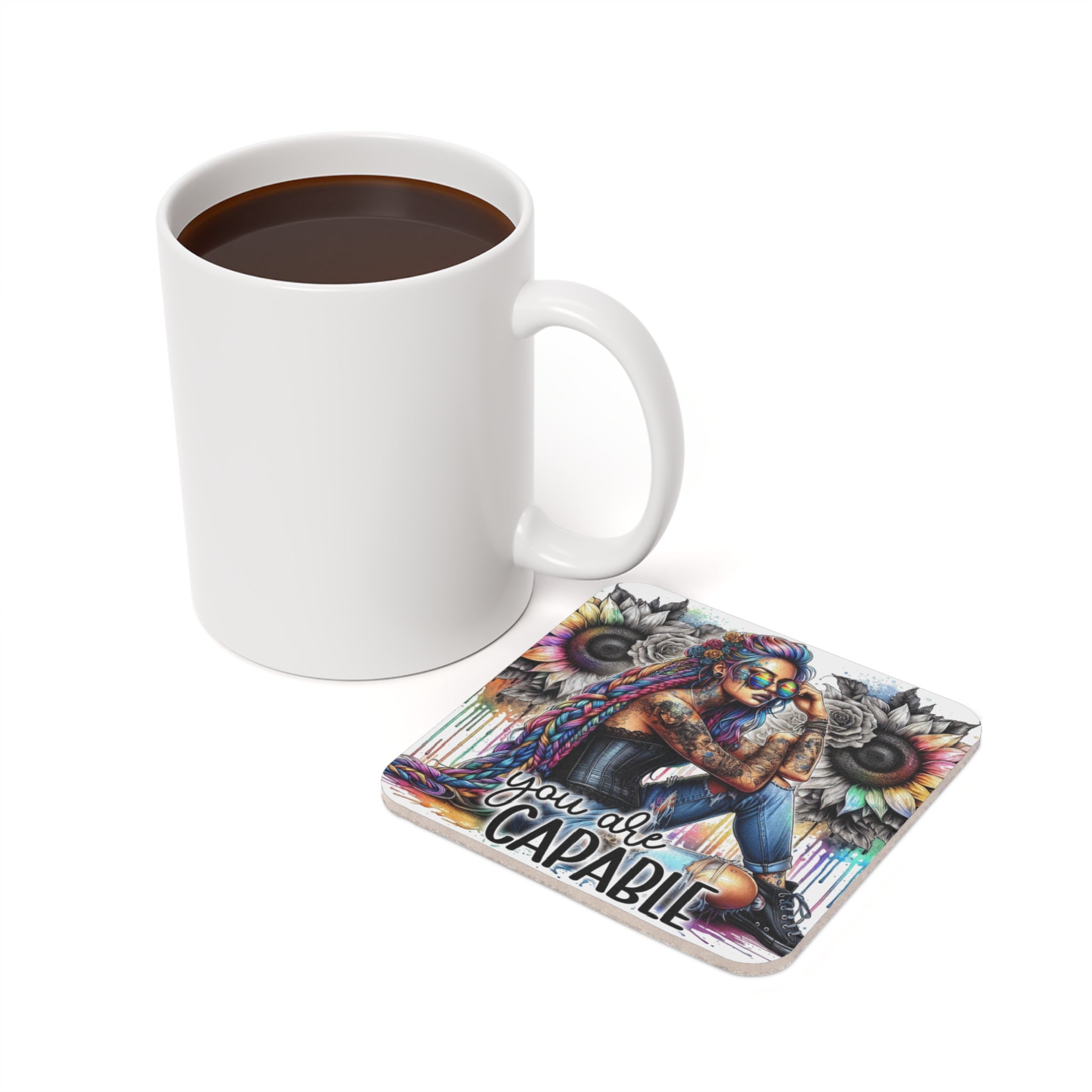 White mug beside a coaster featuring a woman with tattoos and sunflowers, text reads "You are CAPABLE".