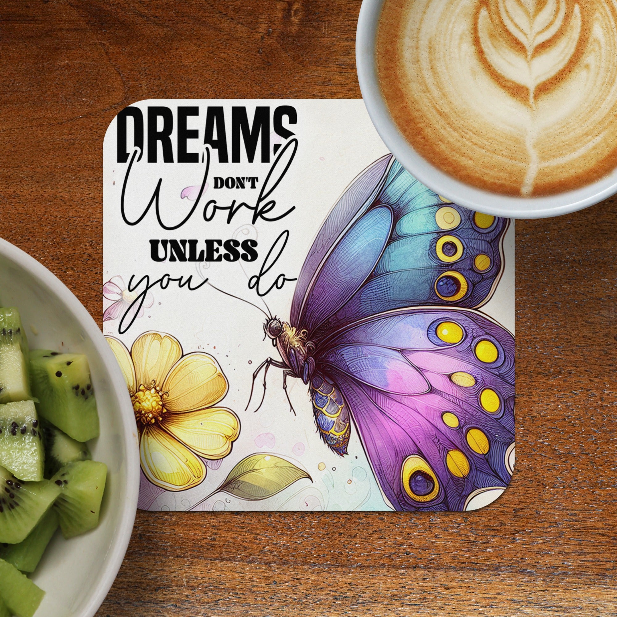 Butterfly and quote "Dream work until you do" on coaster next to kiwi and coffee.