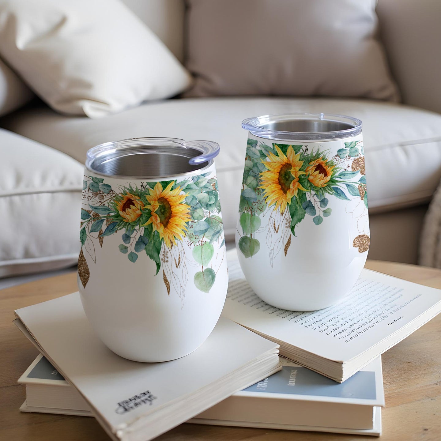 Two insulated tumblers with sunflower and eucalyptus designs rest on books.