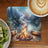Coaster with a campfire scene, log, and coffee.