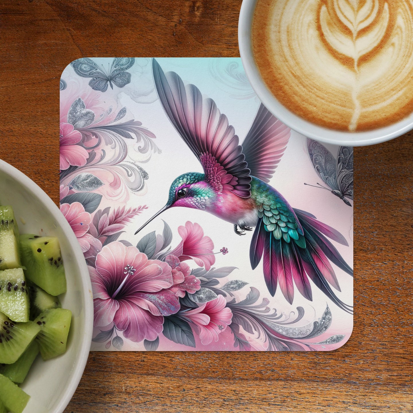 Hummingbird hovering over pink flowers with kiwi slices and coffee.