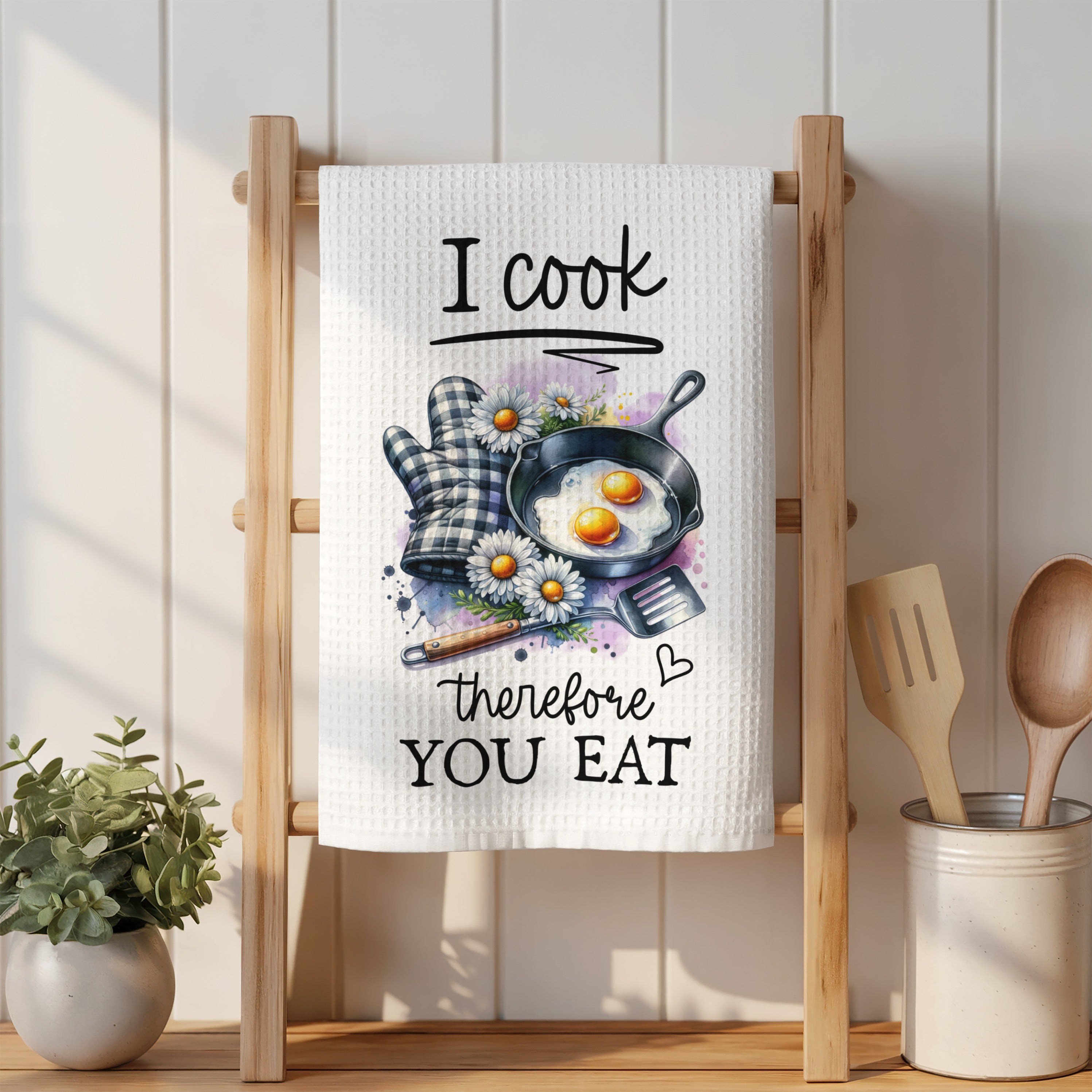 White kitchen towel with "I cook therefore you eat" text, frying pan, and daisies.