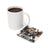 Mug of coffee next to a square coaster with woman and text "Be Kind".