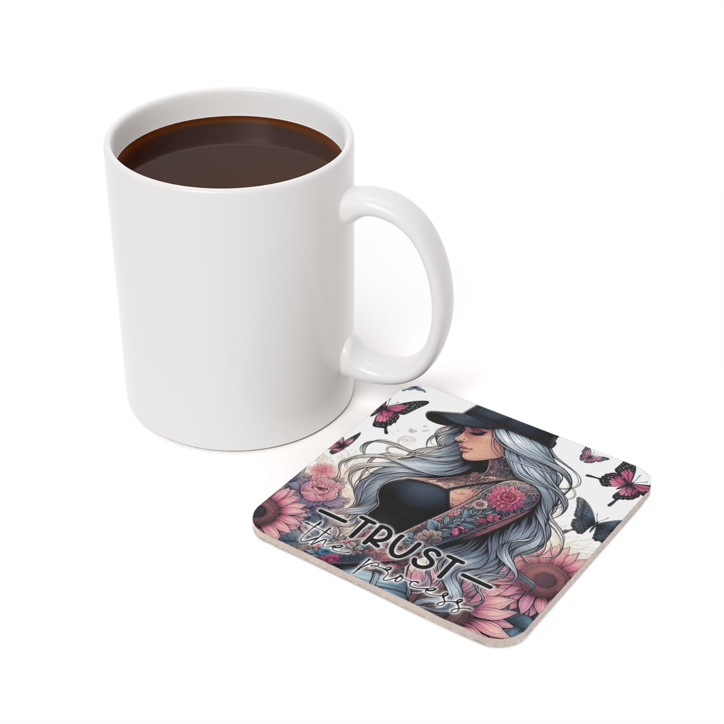 White mug of coffee next to a square coaster with a tattooed woman and "trust the process" text.