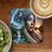 Woman in headdress with eagle and mountainous landscape background, coffee, and kiwi.