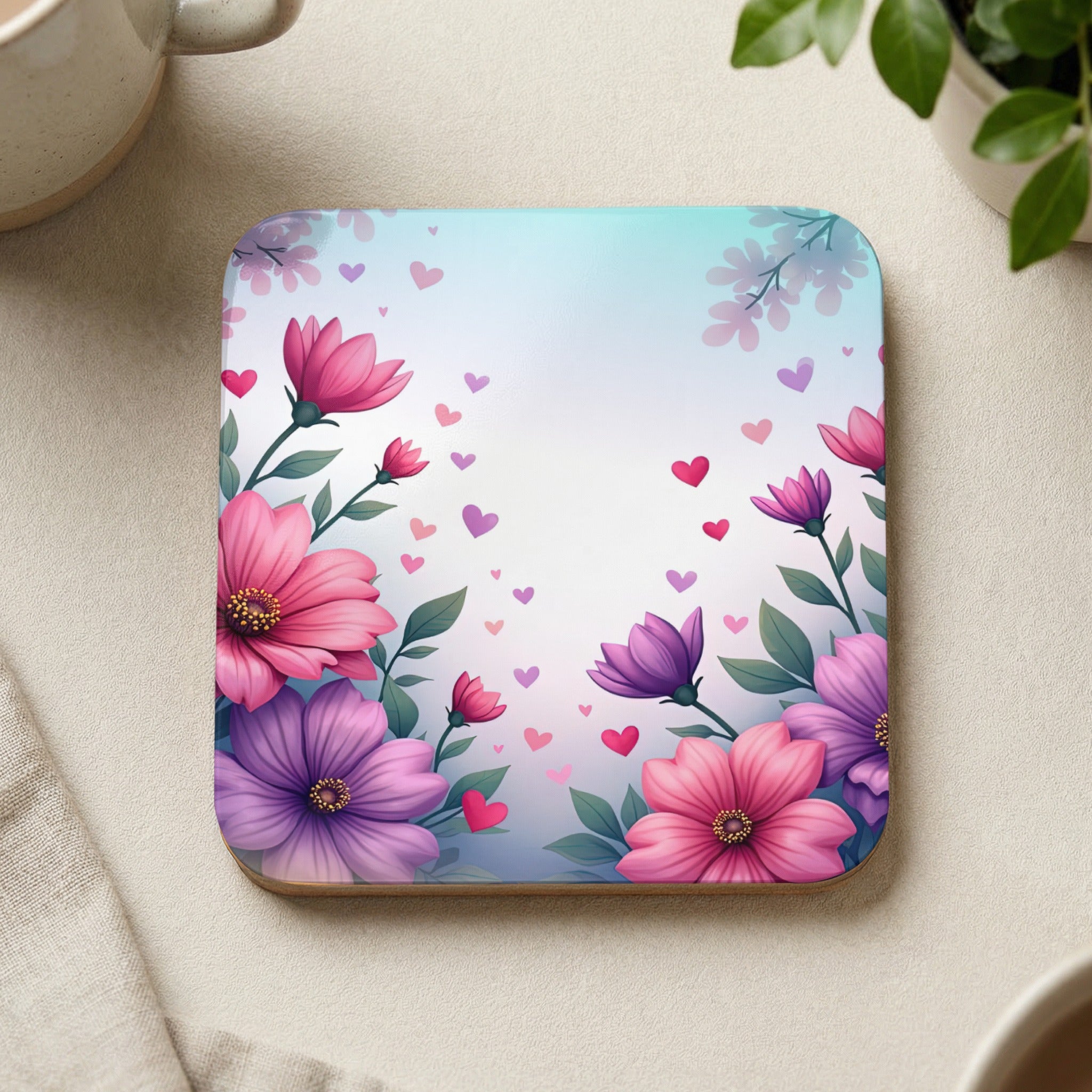 Square coaster with pink and purple flowers and hearts against a soft, blurred background.