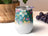 White tumbler with colorful floral pattern, purple grapes, and potted plant background.