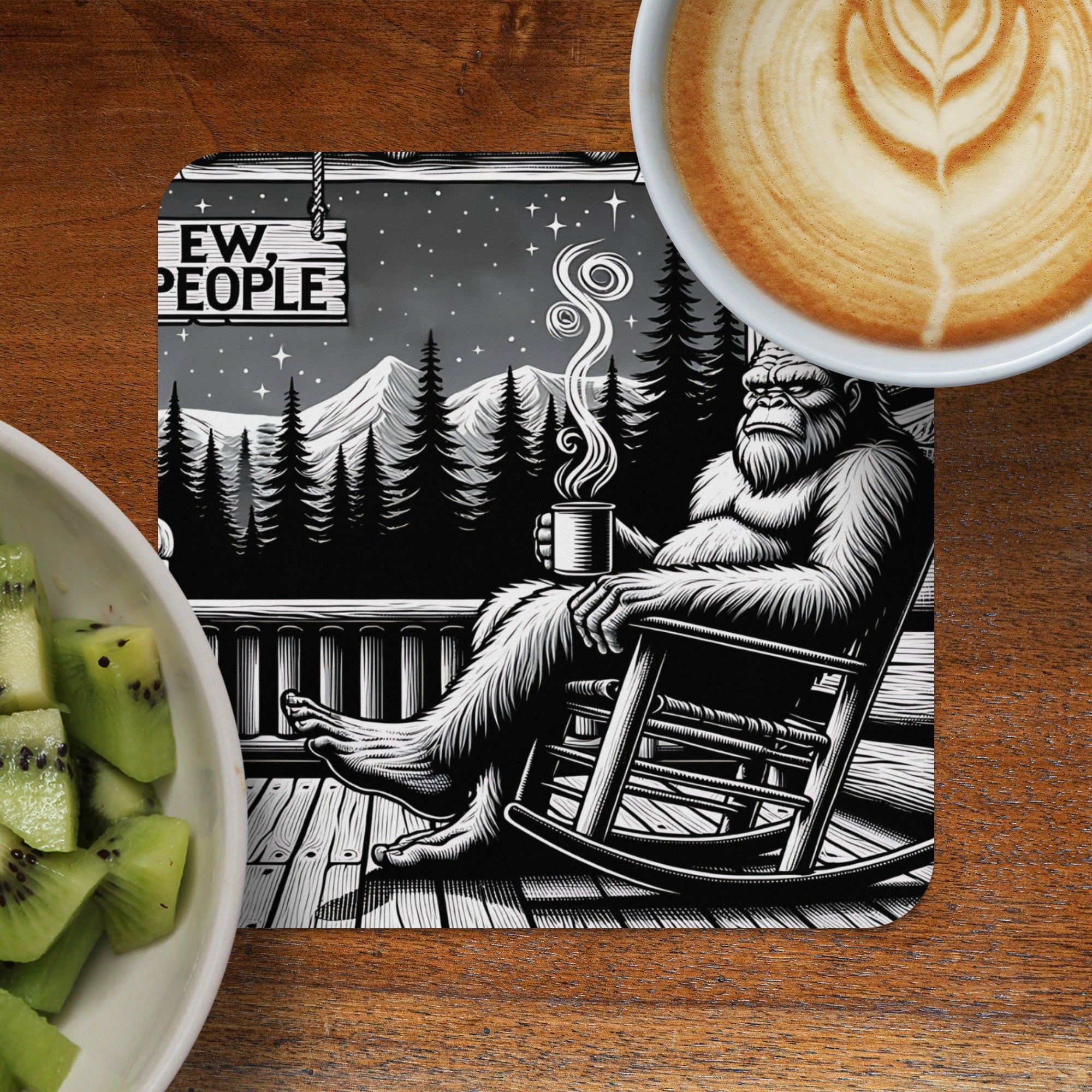 Bigfoot sits in a rocking chair holding a mug, with mountains and trees in background.