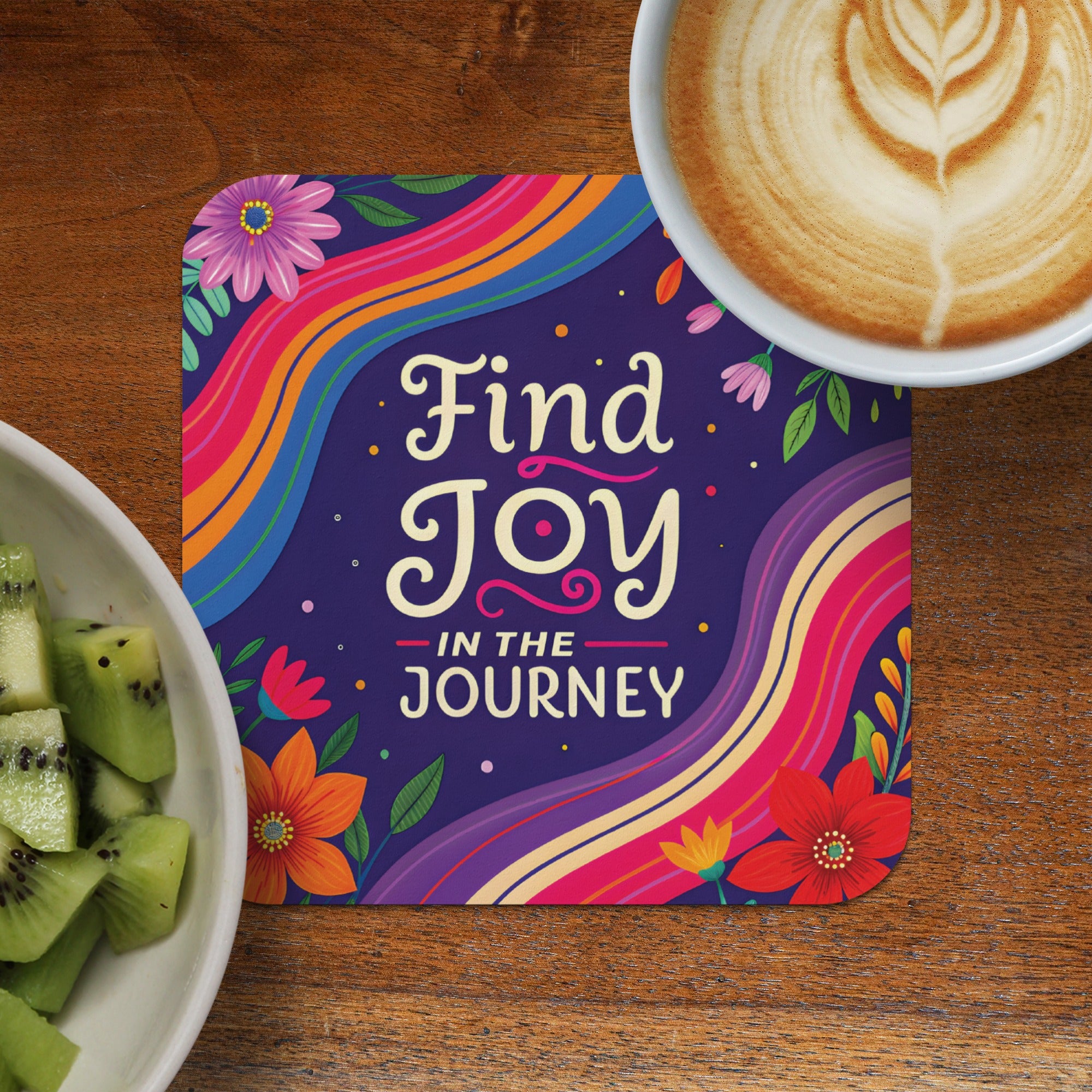 Square coaster with "Find Joy IN THE JOURNEY" text and floral designs, next to kiwi and coffee.