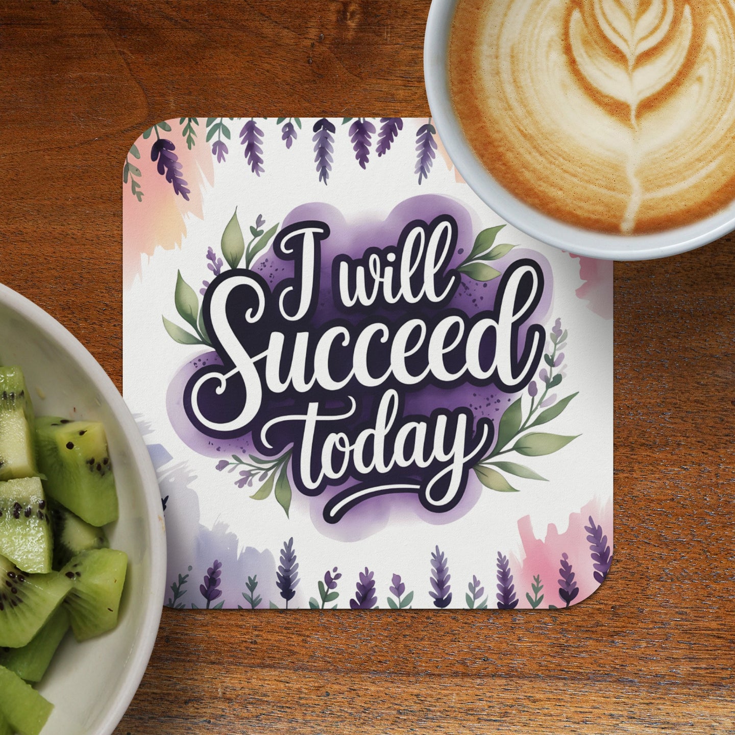 Coaster with "I will succeed today" text and watercolor floral design, next to coffee and kiwi.