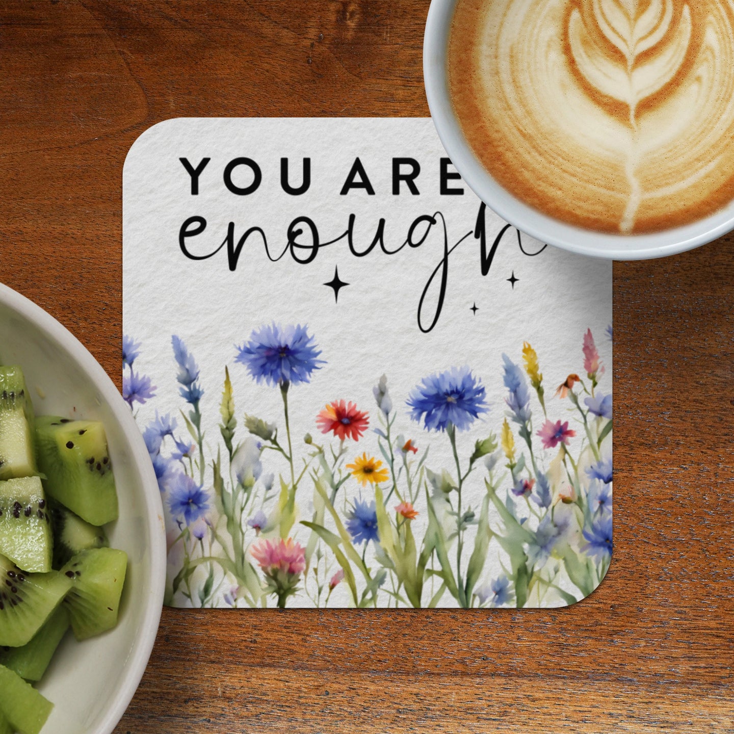White coaster with floral design and "You are enough" text, beside kiwi and coffee.