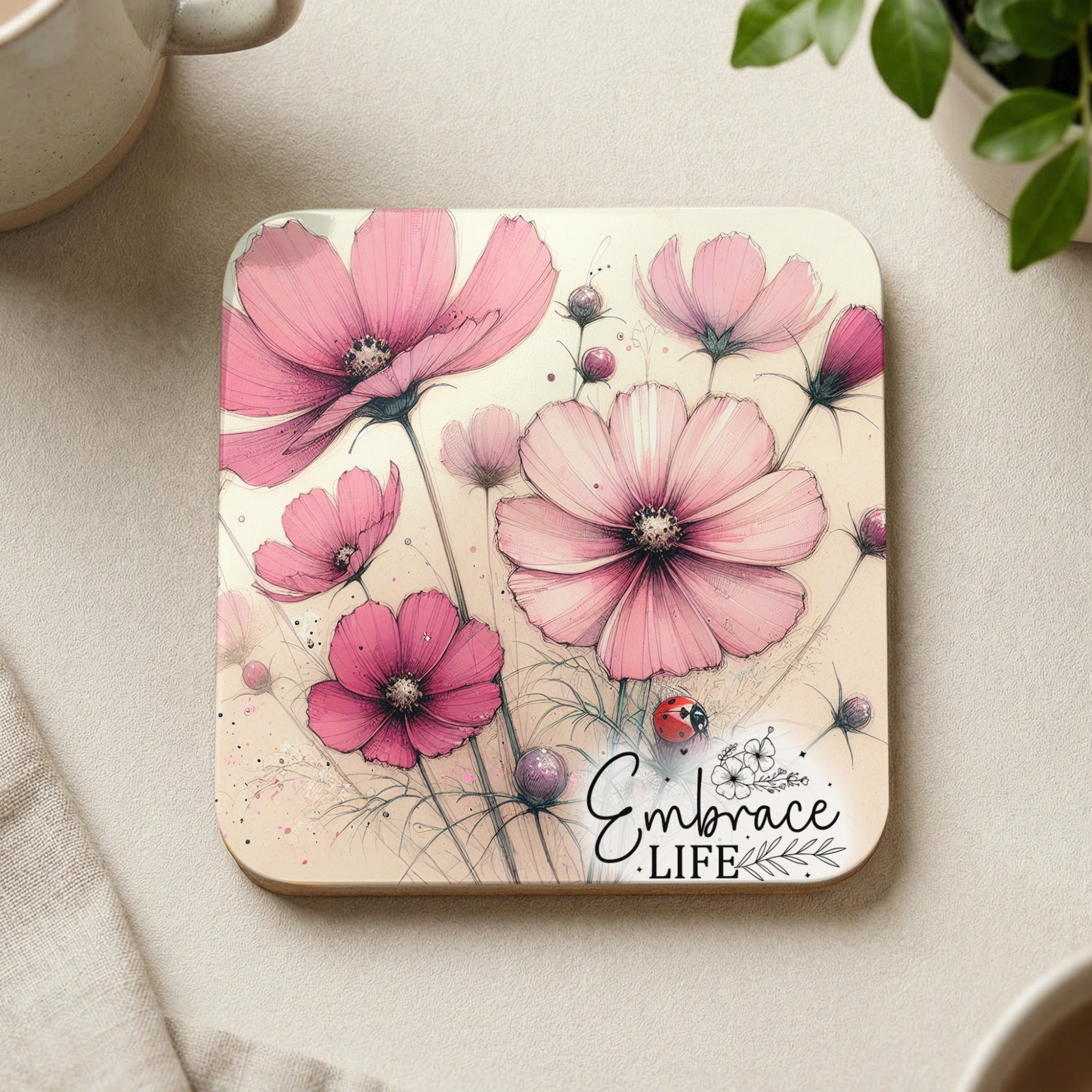 Pink cosmos flowers and a ladybug on a coaster with the text "Embrace Life".