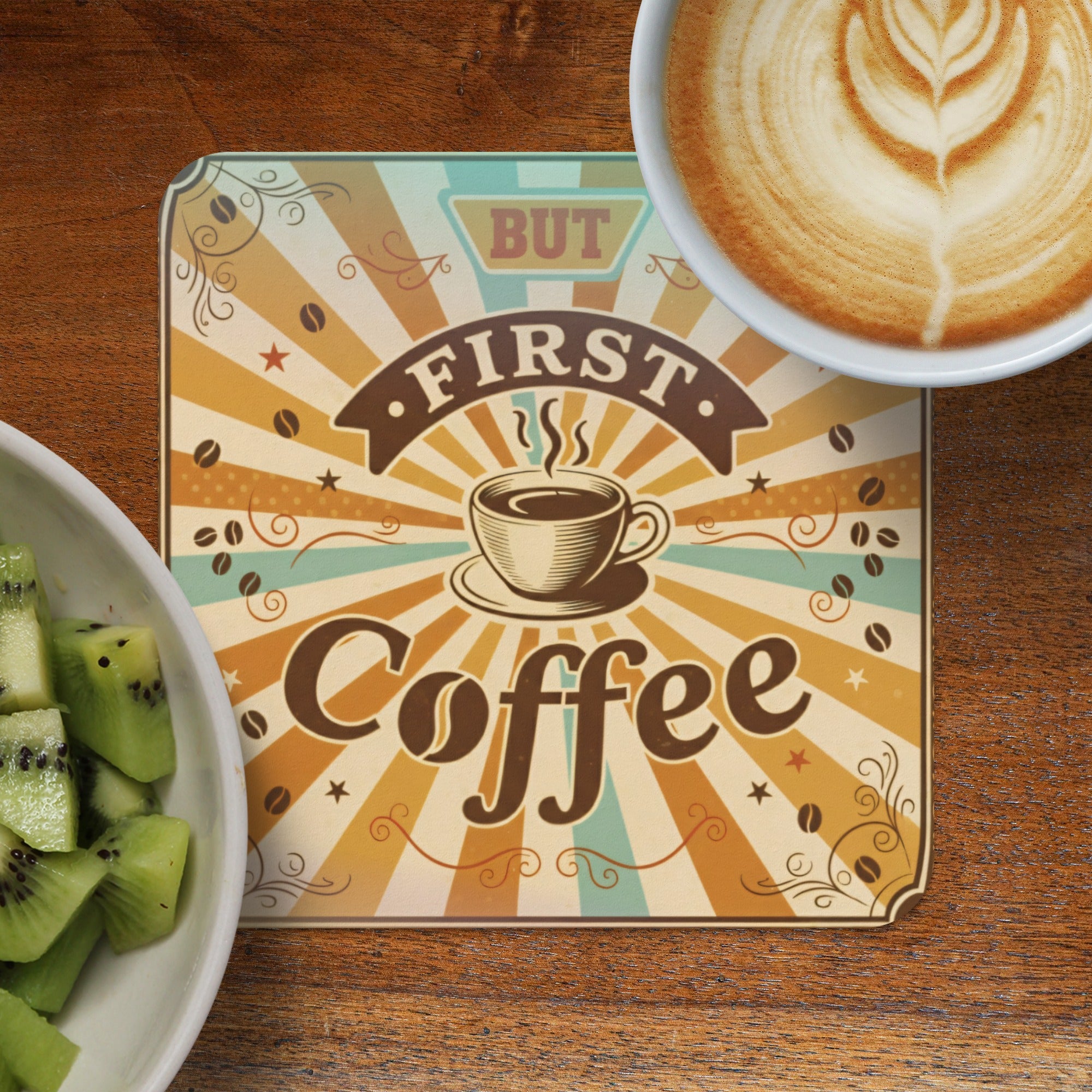 "But First Coffee" sign with latte art and kiwi slices on a wooden table.