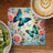 Blue butterflies and roses on a placemat next to a coffee and kiwi.