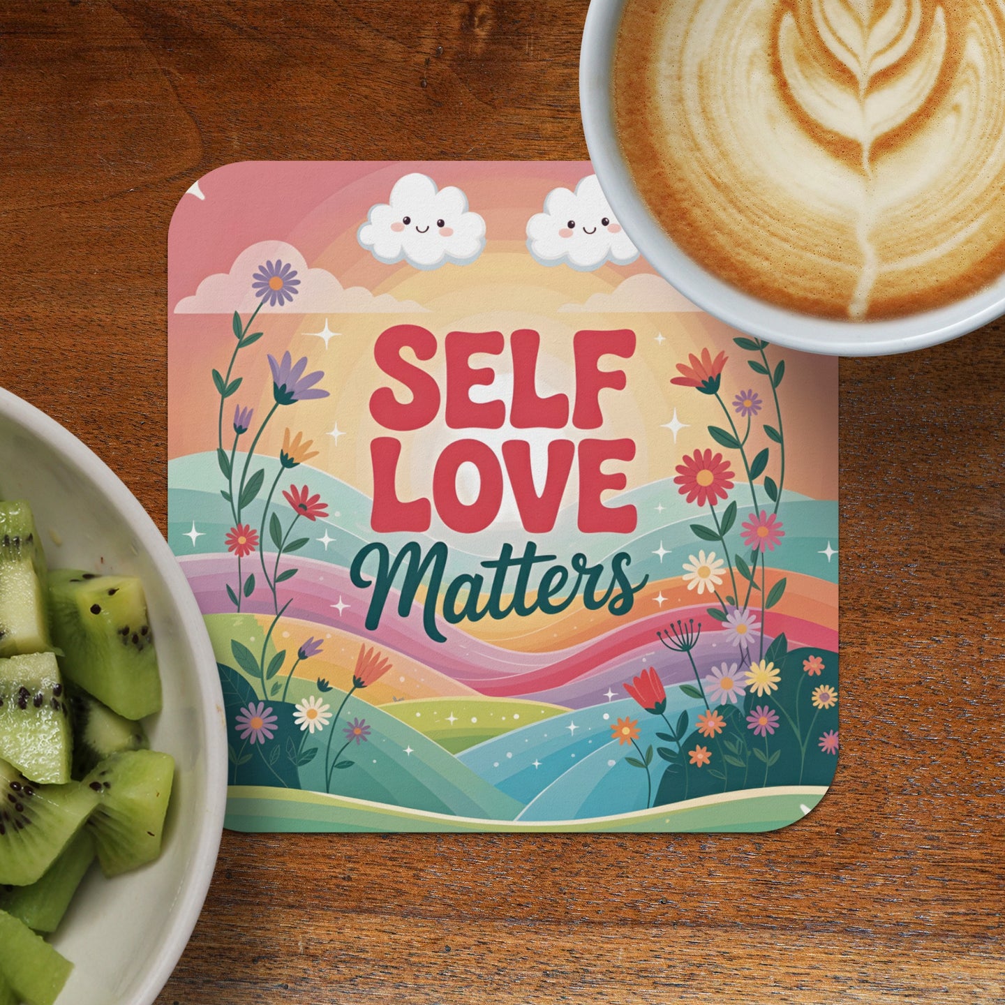 Coaster with "Self Love Matters" text, floral and cloud design, next to kiwi and coffee.